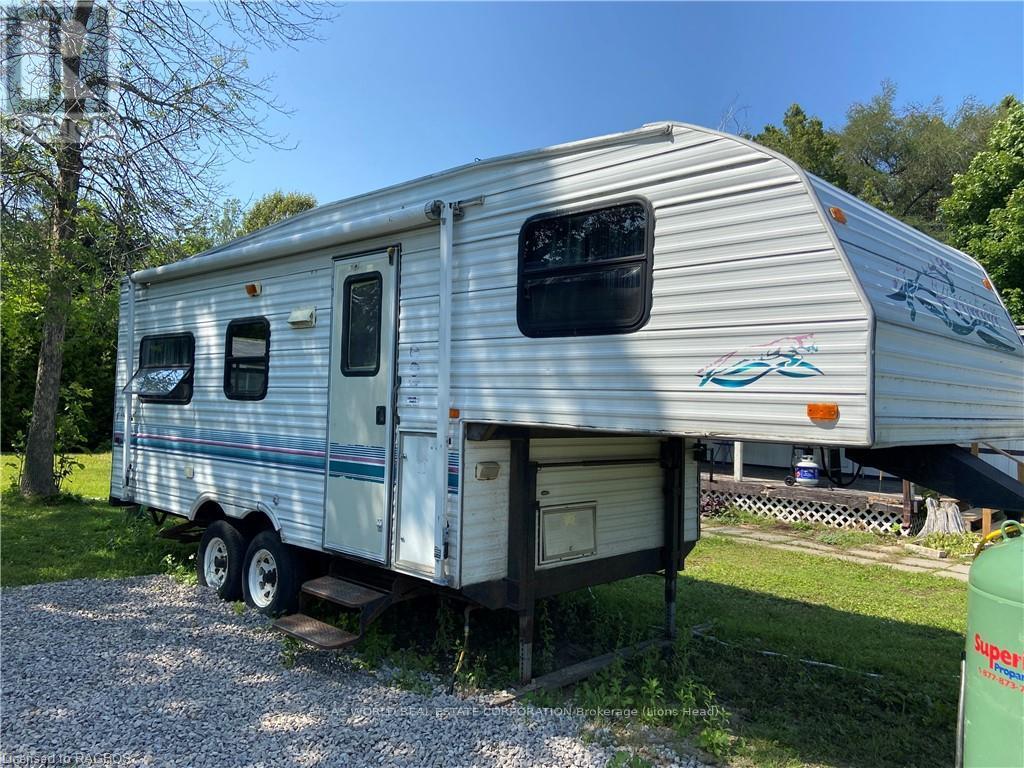 A silver RV is parked on a gravel area.