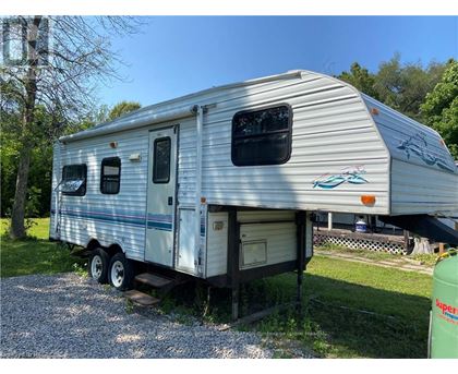 A silver RV is parked on a gravel area.