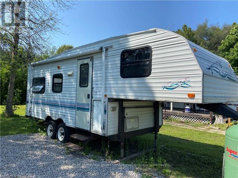 A silver RV is parked on a gravel area.