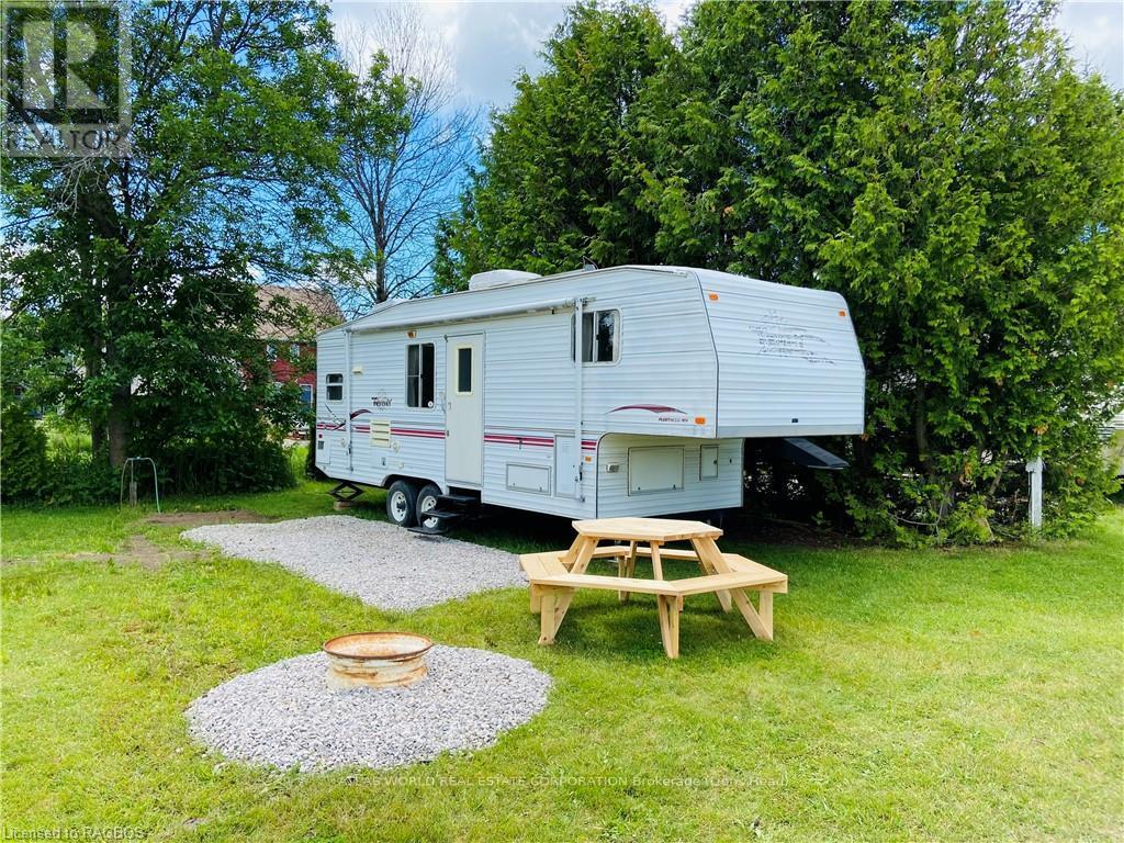 A white RV is parked in a grassy area with a picnic table and a fire pit nearby.
