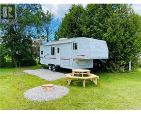A white RV is parked in a grassy area with a picnic table and a fire pit nearby.