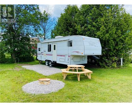 A white RV is parked in a grassy area with a picnic table and a fire pit nearby.