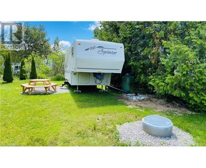 A white Sprinter RV is parked in a grassy area with a picnic table and a gravel pit.
