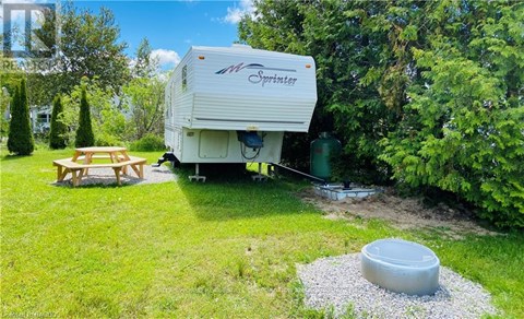 A white Sprinter RV is parked in a grassy area with a picnic table and a gravel pit.