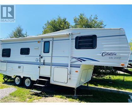 A white RV with a blue stripe and the word "Citilon" on it is parked on grass.