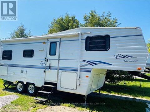 A white RV with a blue stripe and the word "Citilon" on it is parked on grass.