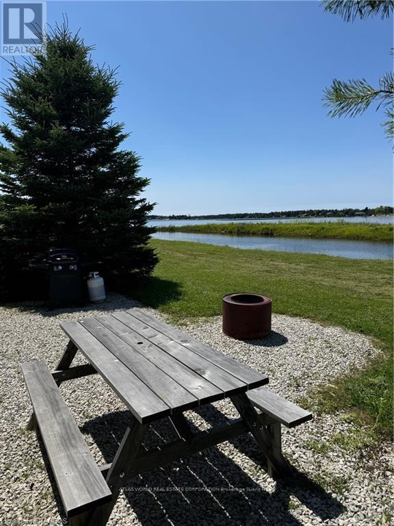 A picnic table sits on a gravel area next to a tree and a body of water.
