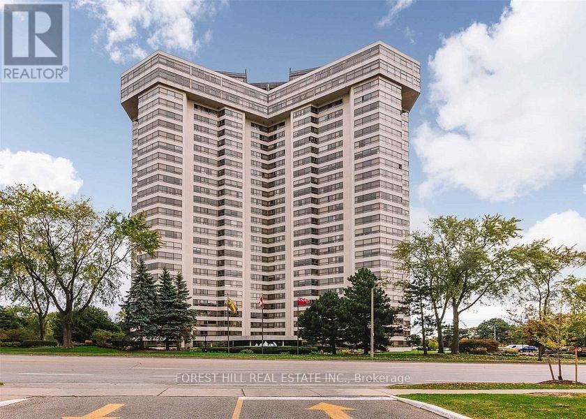 A tall building with a glass facade is surrounded by trees and grass.