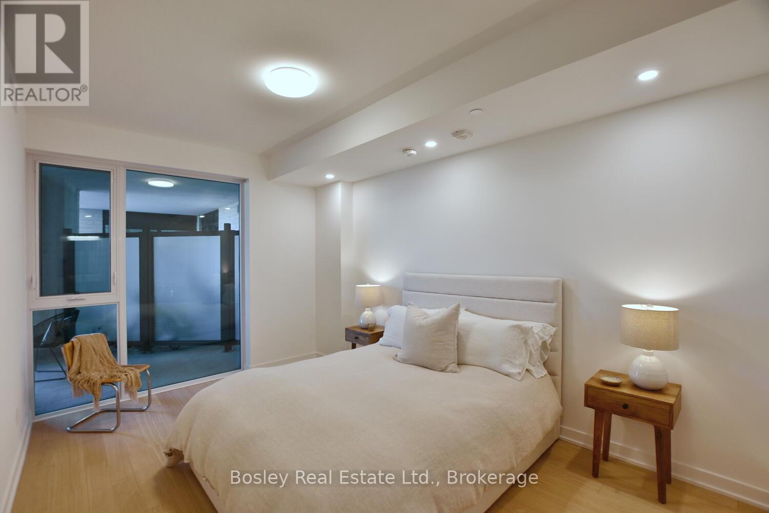 A bedroom with a bed, a chair, and a table with a lamp on it.