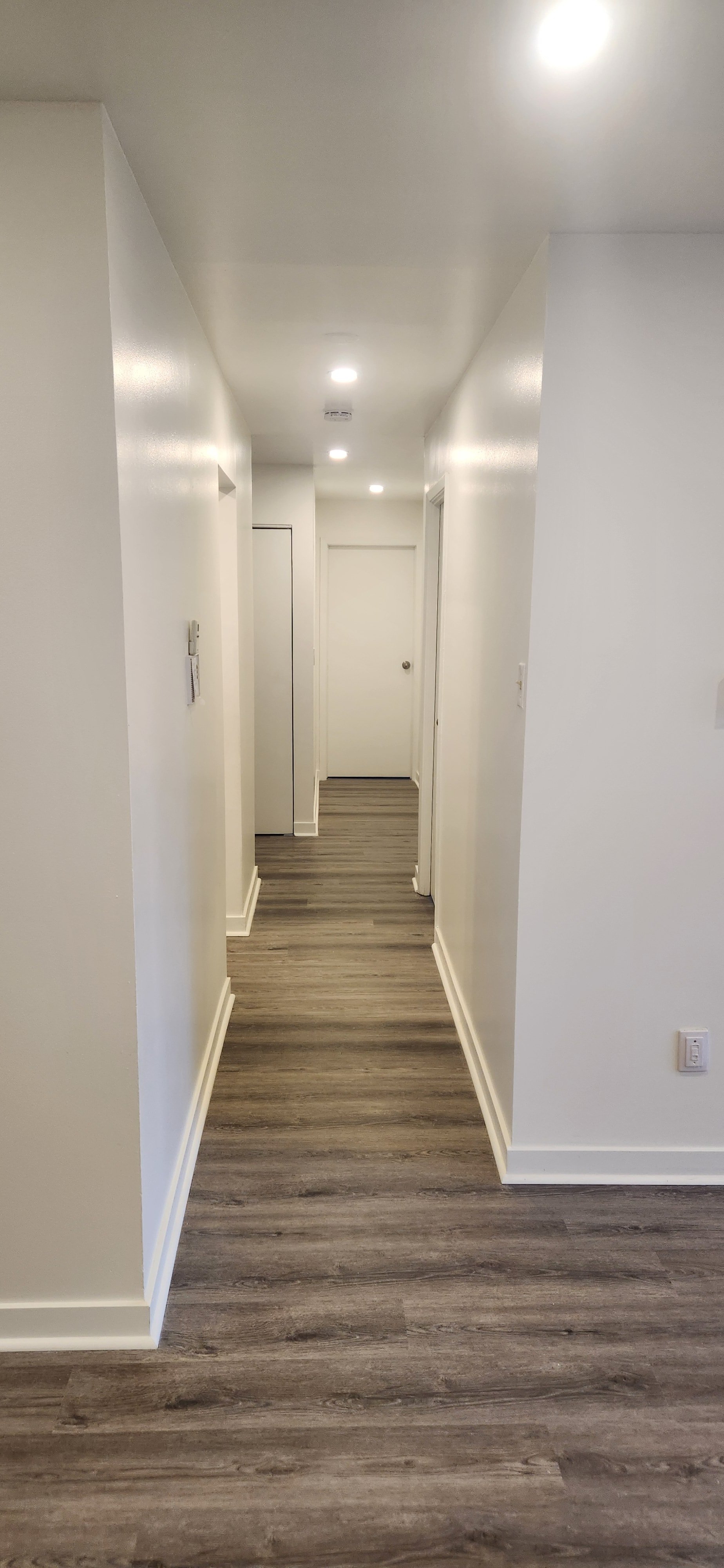 A long hallway with white walls and carpeted flooring.