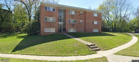 A red brick apartment building with a green lawn in front.