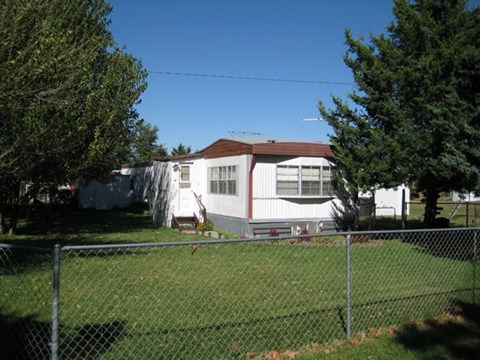A white house with a brown roof is surrounded by a chain link fence.