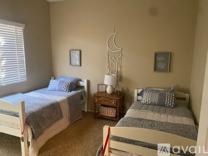 A bedroom with two beds, one with a blue comforter and the other with a grey comforter, a nightstand with a lamp, and a wall hanging.