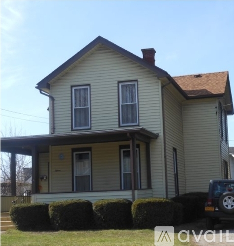 A two-story house with a porch and a car parked in front.