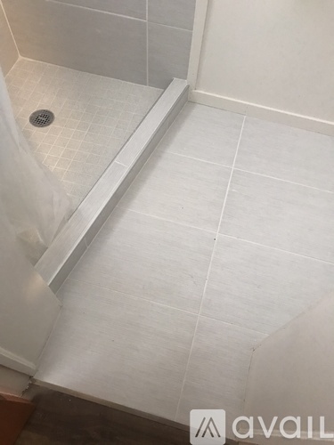 A bathroom with a white tiled floor and a drain in the corner.