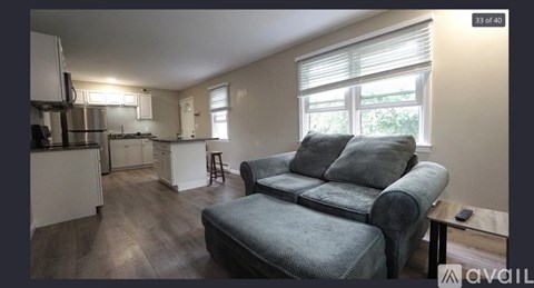 A living room with a grey couch and a kitchen area in the background.