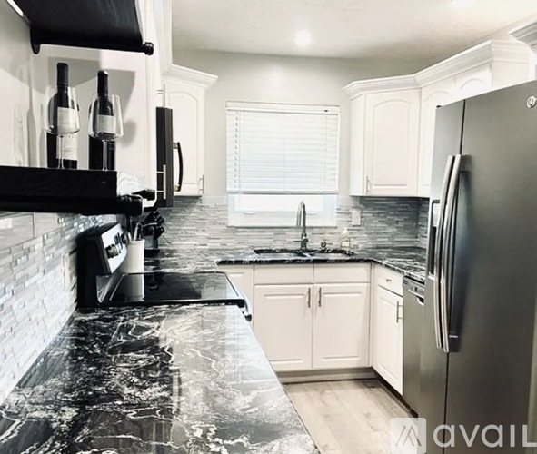 A kitchen with a black marble countertop and a stainless steel refrigerator.
