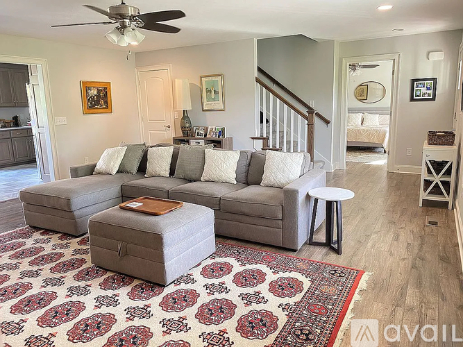 A living room with a grey couch and a rug with a red and black design.