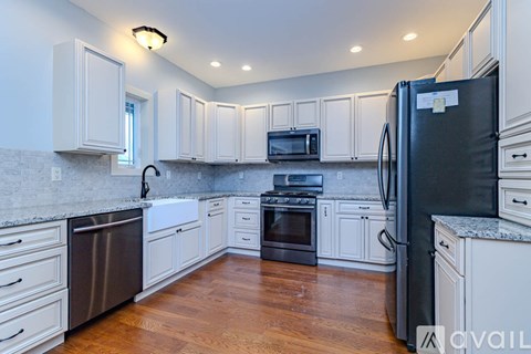 A black refrigerator in a kitchen with wooden floors and a wooden railing.