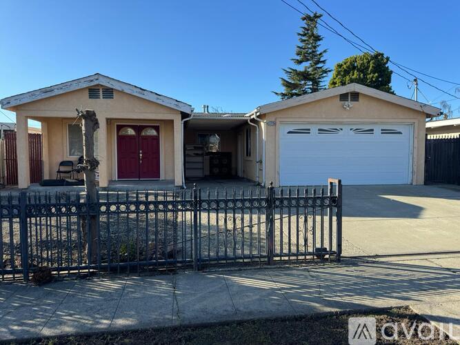 A house with a red door and a garage door is surrounded by a black metal fence.