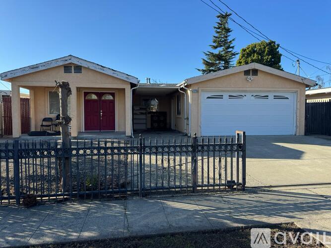 A two-story house with a red door and a garage door is surrounded by a black metal fence.