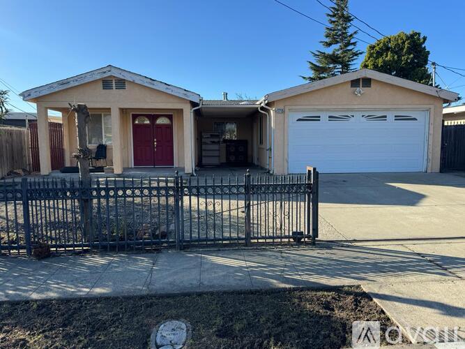 A house with a red door and a white garage door is surrounded by a black metal fence.
