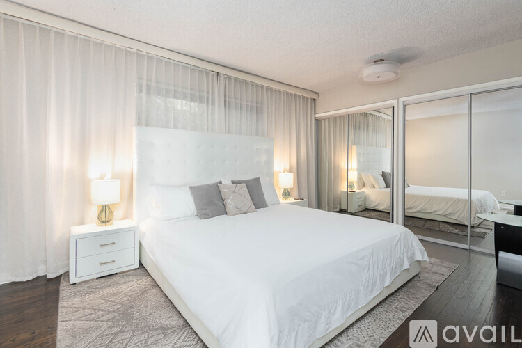 A bedroom with a large bed, a nightstand with a lamp, and a mirrored closet door.