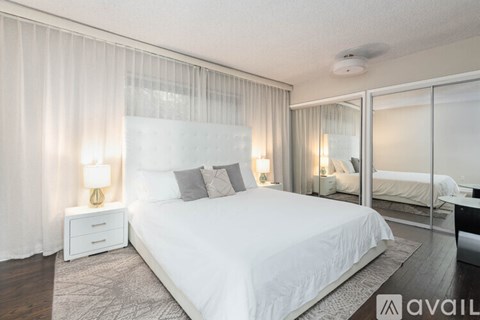 A bedroom with a large bed, a nightstand with a lamp, and a mirrored closet door.