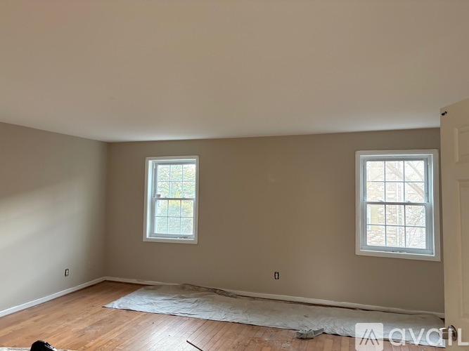 A room with two windows and wooden floors under construction.