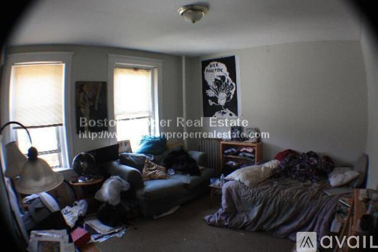 A cluttered room with a bed, couch, and lamp.