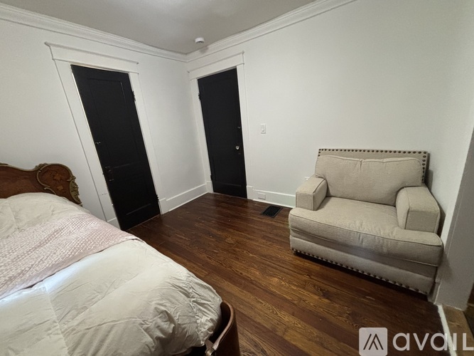 A bedroom with a bed, chair, and wooden floors.