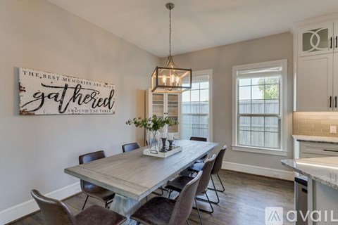 A dining room with a wooden table and chairs, a hanging light fixture, and a sign that says "The best memories are made around the table.".