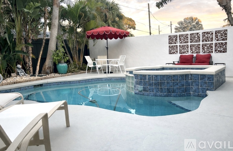A pool with a red umbrella and white chairs.