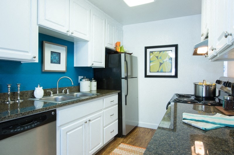 Sienna Apartments, kitchen area with a dishwasher a stainless steel fridge white cabinets and blue backsplash wall