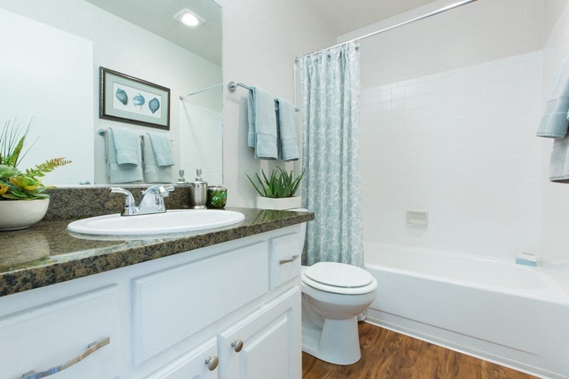 Sienna apartments with white bathroom a teal shower curtain and a brown countertop placed on white cabinets.