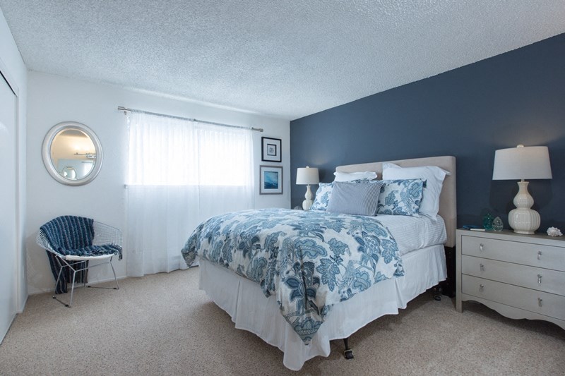 Sienna apts bedroom with a dark teal wall a bed placed int he middle of two white nightstands with blue flower bedspread.