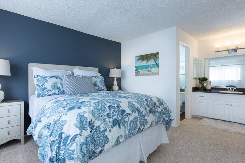 Sienna apts bedroom with a dark teal wall a bed placed int he middle of two white nightstands with blue flower bedspread.
