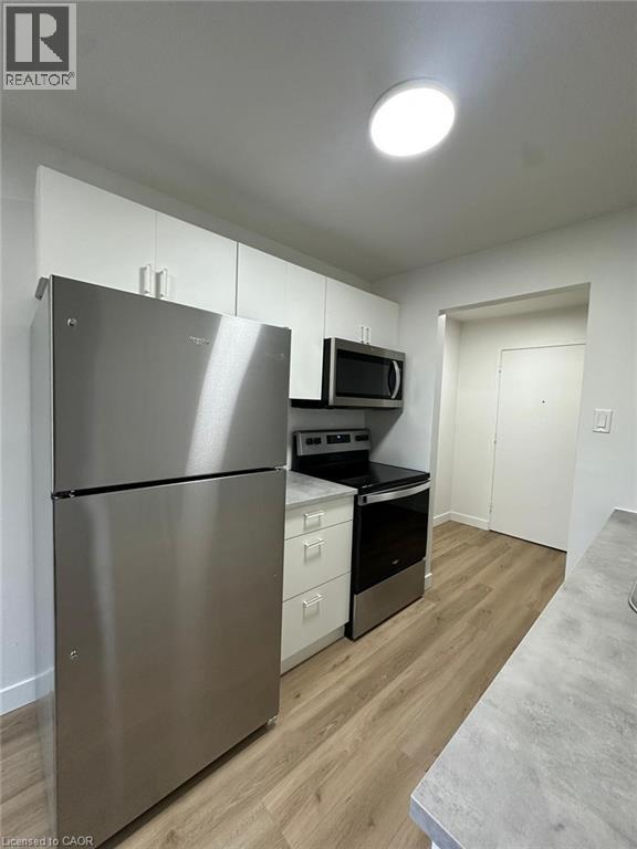 A stainless steel refrigerator is in a kitchen with wood floors and white walls.