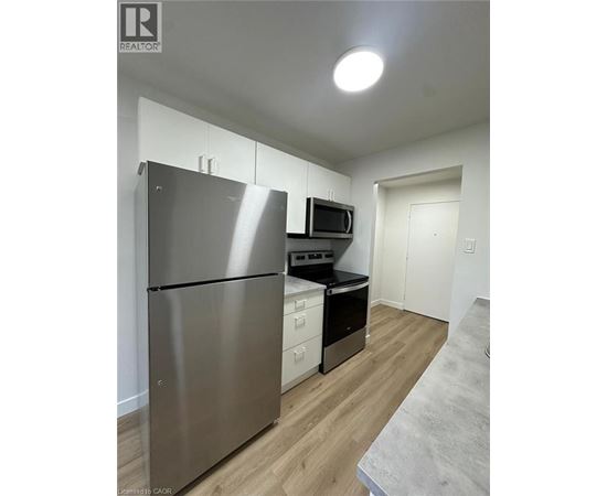 A stainless steel refrigerator is in a kitchen with wood floors and white walls.