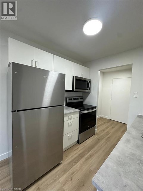 A stainless steel refrigerator is in a kitchen with wood floors and white walls.