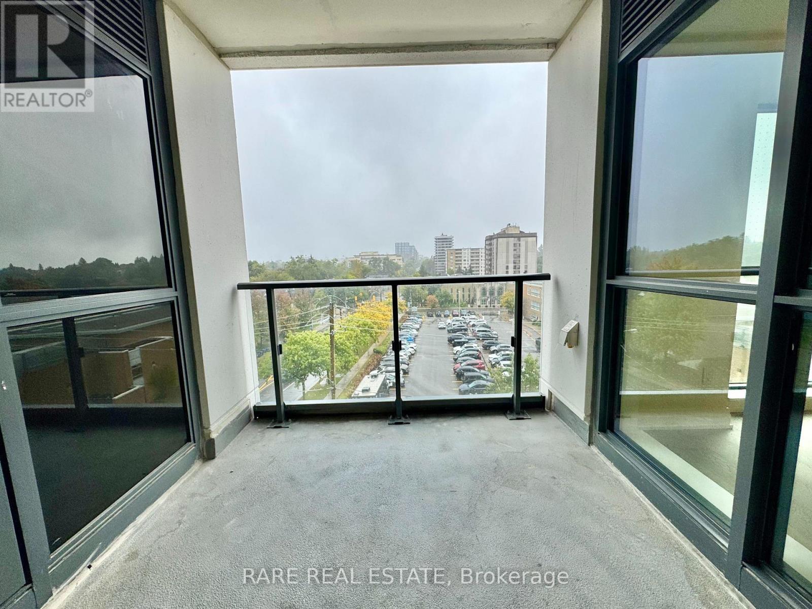 A balcony with glass doors overlooking a parking lot and buildings.