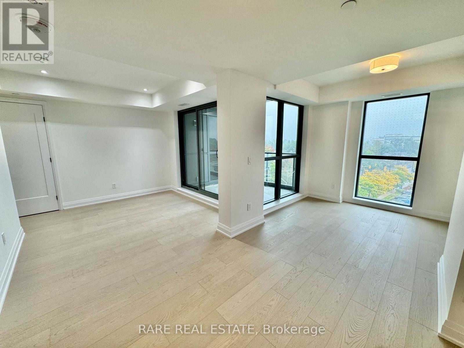 A spacious room with wooden flooring and large windows.