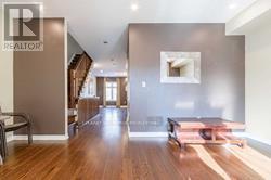 A spacious room with a wooden floor and a staircase in the background.