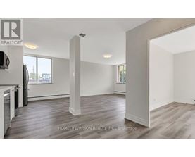 A spacious room with wooden flooring and white walls, part of a real estate listing.
