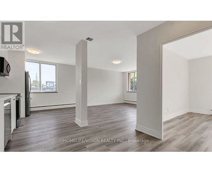 A spacious room with wooden flooring and white walls, part of a real estate listing.