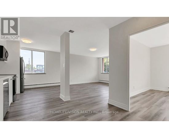 A spacious room with wooden flooring and white walls, part of a real estate listing.