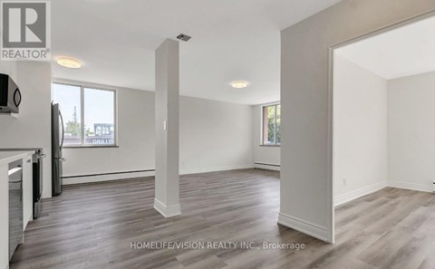 A spacious room with wooden flooring and white walls, part of a real estate listing.