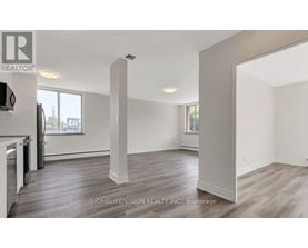 A realtor photo of a large empty room with wood floors and white walls.