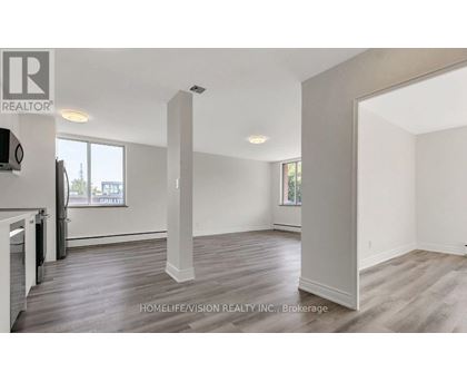 A realtor photo of a large empty room with wood floors and white walls.