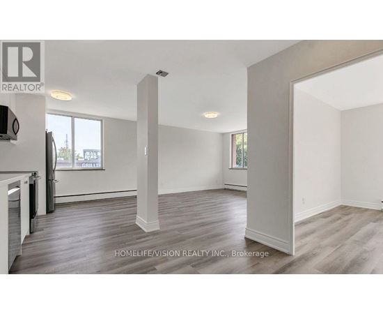 A realtor photo of a large empty room with wood floors and white walls.